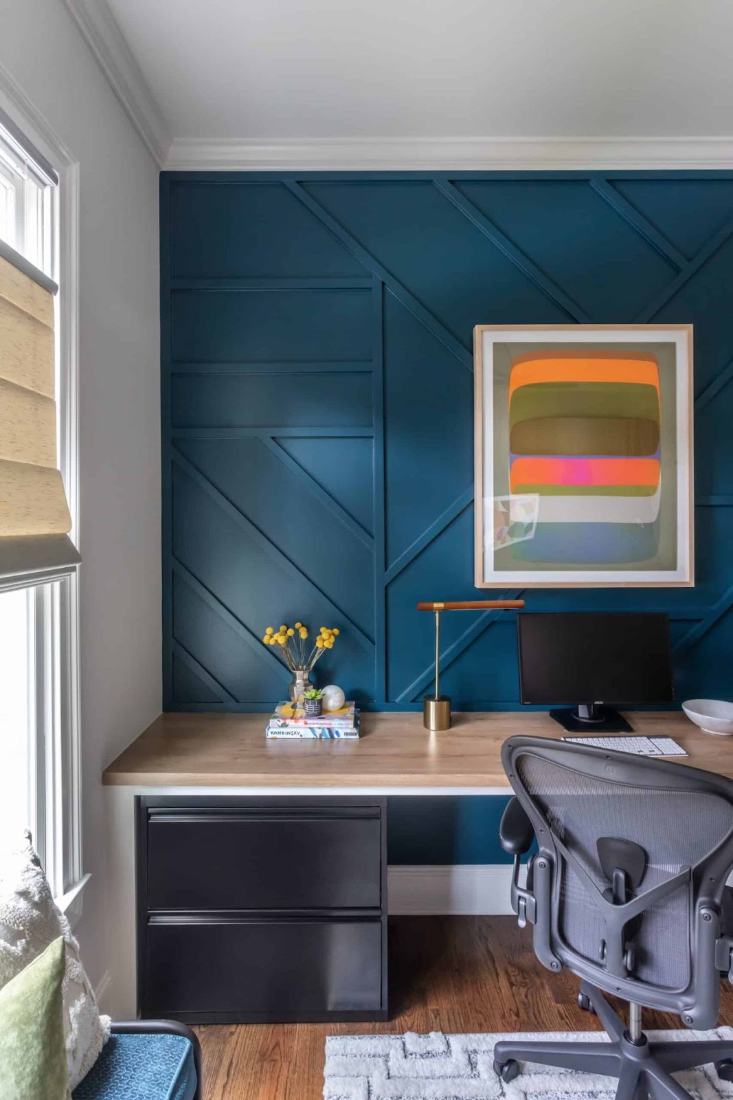 Office with blue accent wall, black office chair, and orange, pink, and green abstract art. 