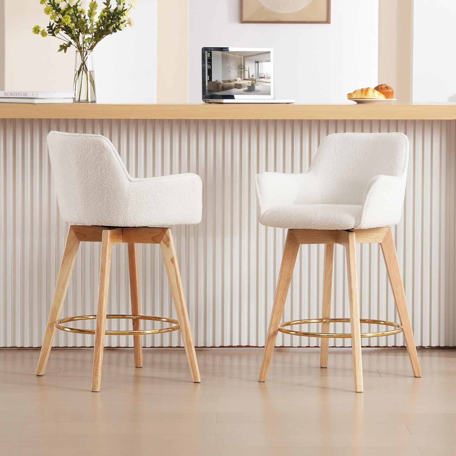 Two boucle bar stools with wooden legs and gold footrests placed in front of sleek kitchen counter.