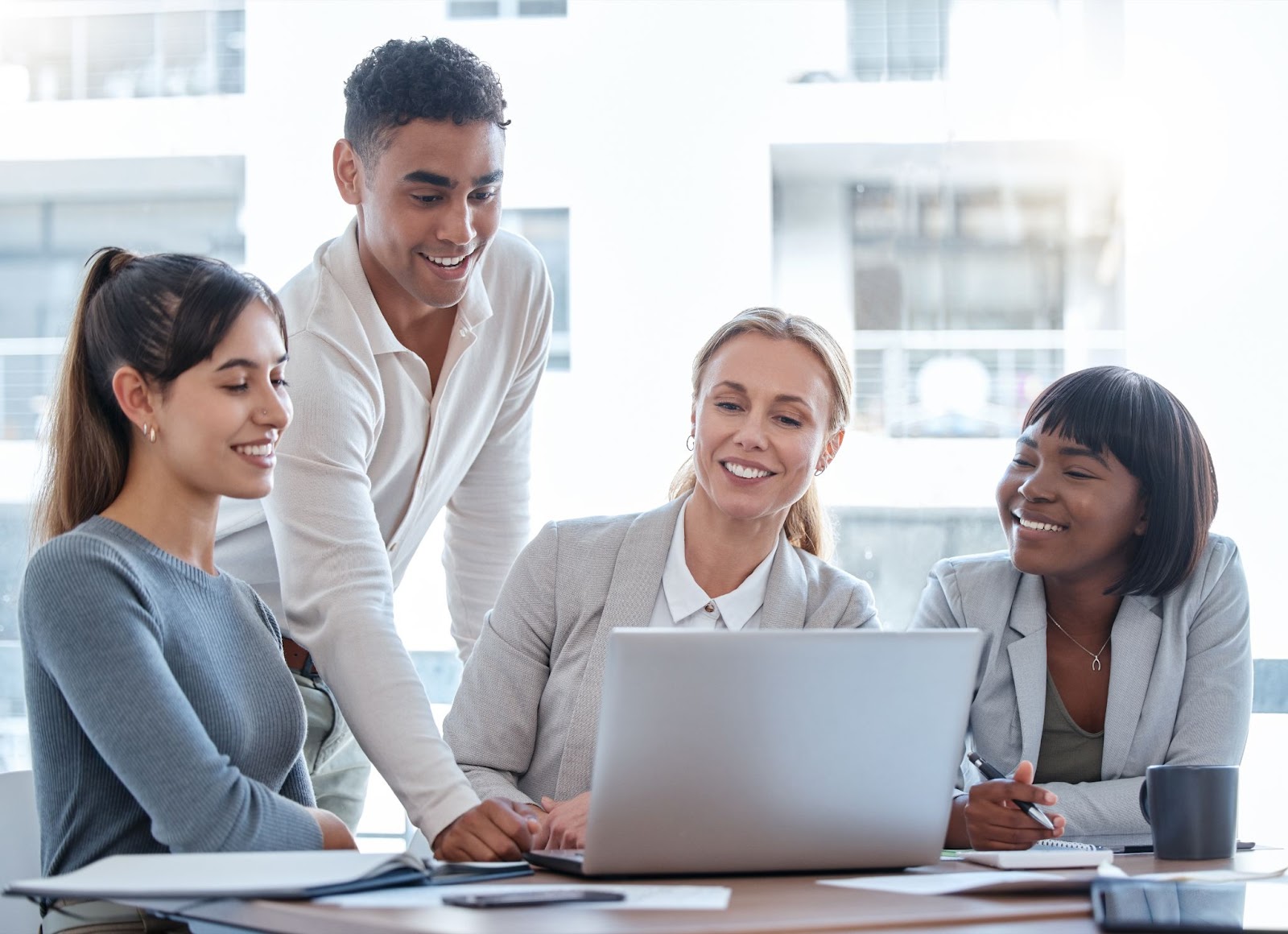 Three women and one man are smiling and looking at a laptop. 