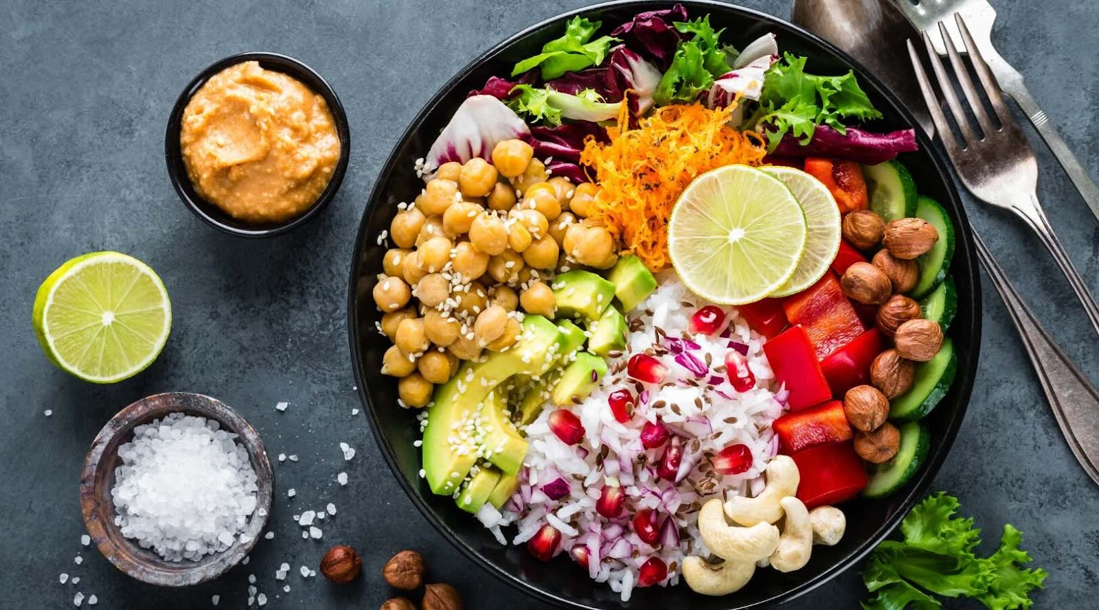 Healthy vegetarian Buddha bowl with chickpeas, avocado, rice, pomegranate seeds, cashews, and a variety of fresh vegetables, topped with a lime slice and served with a side of dipping sauce. This colorful and nutritious dish is perfect for anyone looking to enjoy a balanced meal, recommended by our registered dietitian in Mississauga.