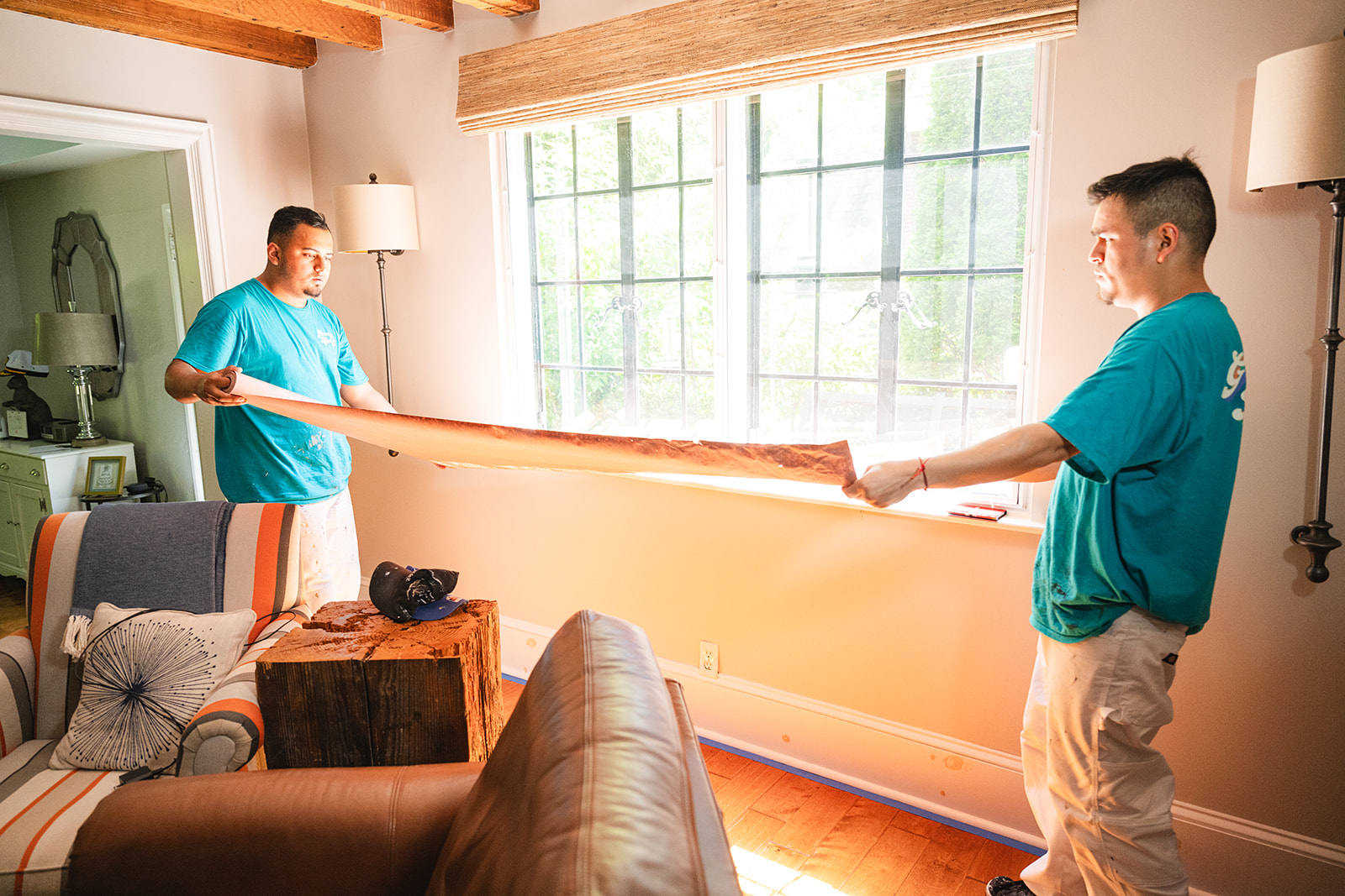 Two Groovy Hues Painting of Philadelphia team members carefully preparing a room for painting in Main Line, PA, covering a window with protective paper.