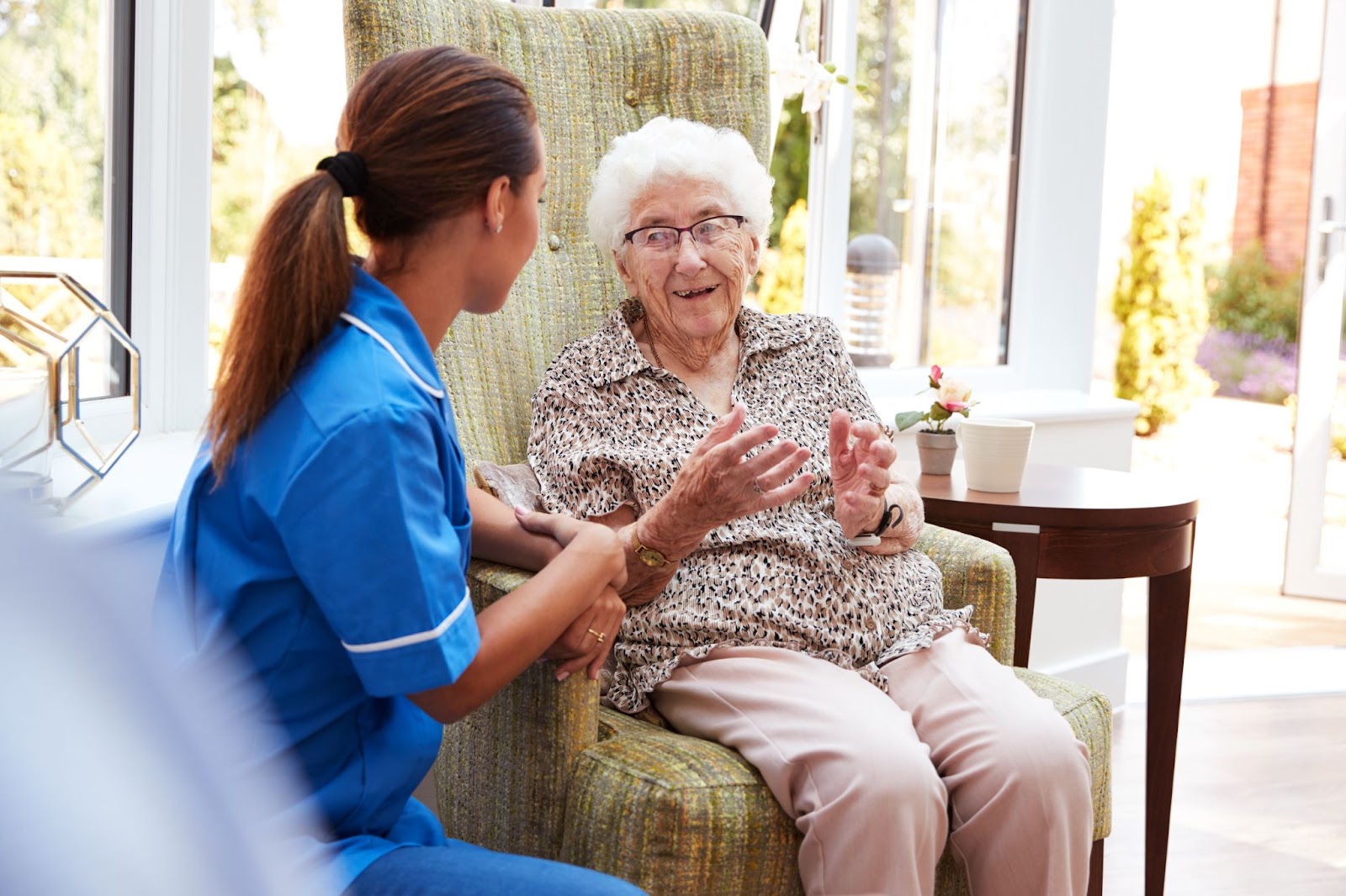 An older adult sitting in a chair talking to a staff member during a visit to a memory care facility.