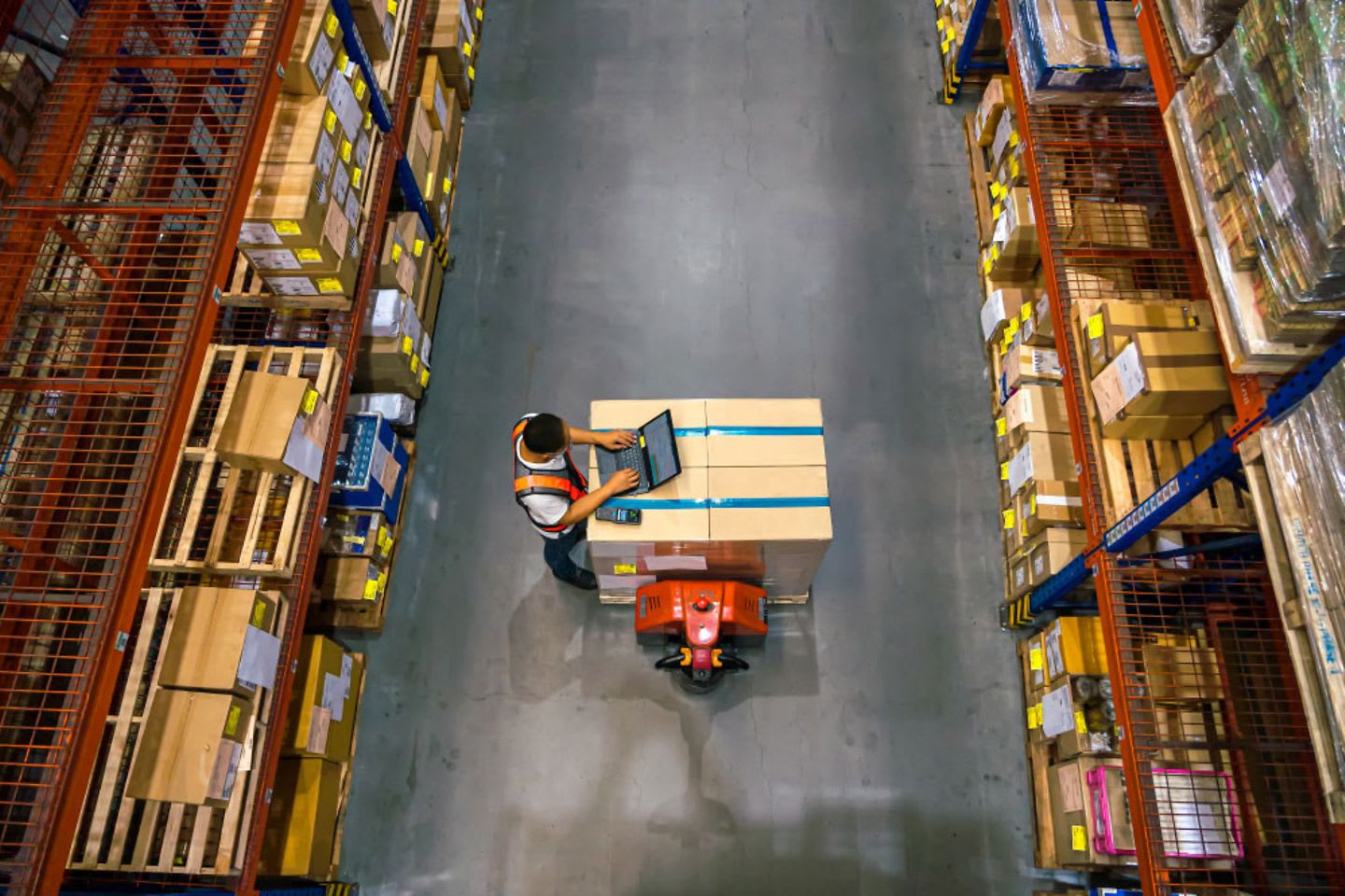 A worker uses a laptop for inventory management in a busy warehouse, highlighting the central role of secure warehousing in supply chain operations