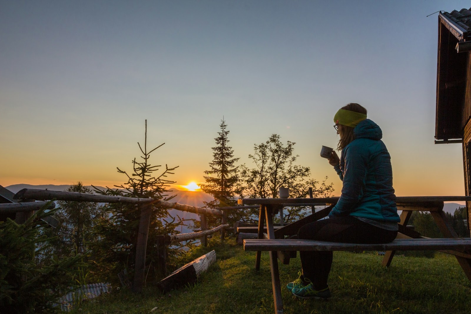 A woman sitting on a park bench during the sunrise drinking a coffee