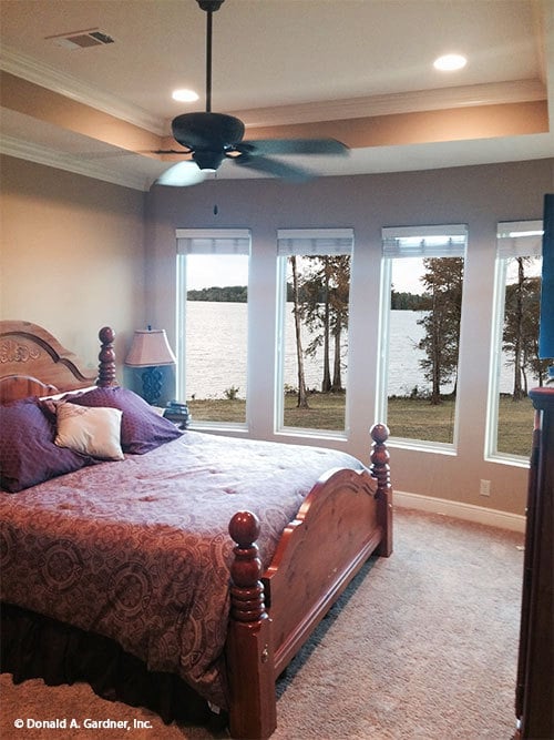 Primary bedroom with a tray ceiling, carpet flooring, and a bow window overlooking the nearby lake.