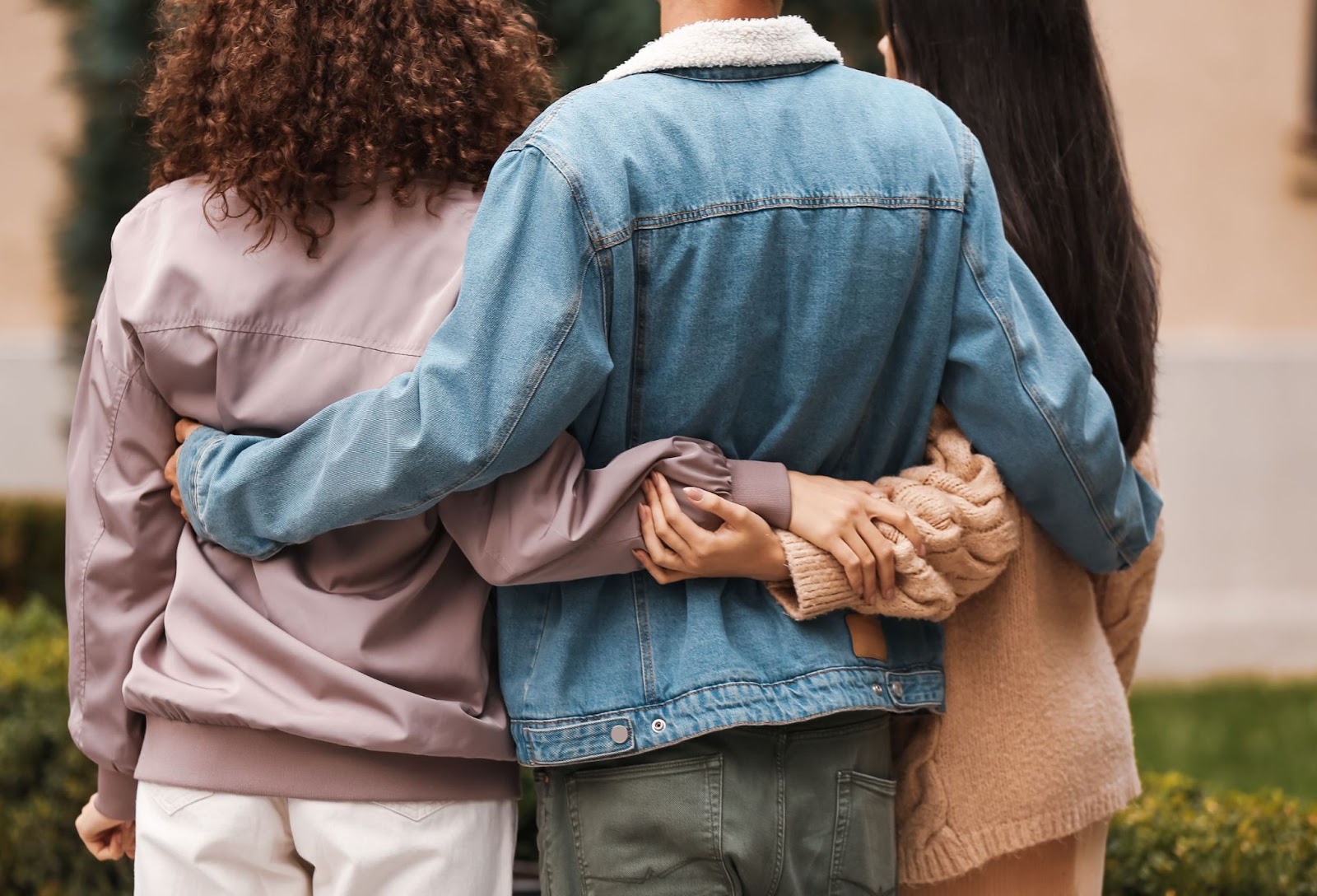 Duas mulheres e um homem no meio de costas, os três estão se abraçando