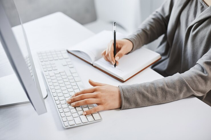 Person writing a blog entry on a notebook while typing