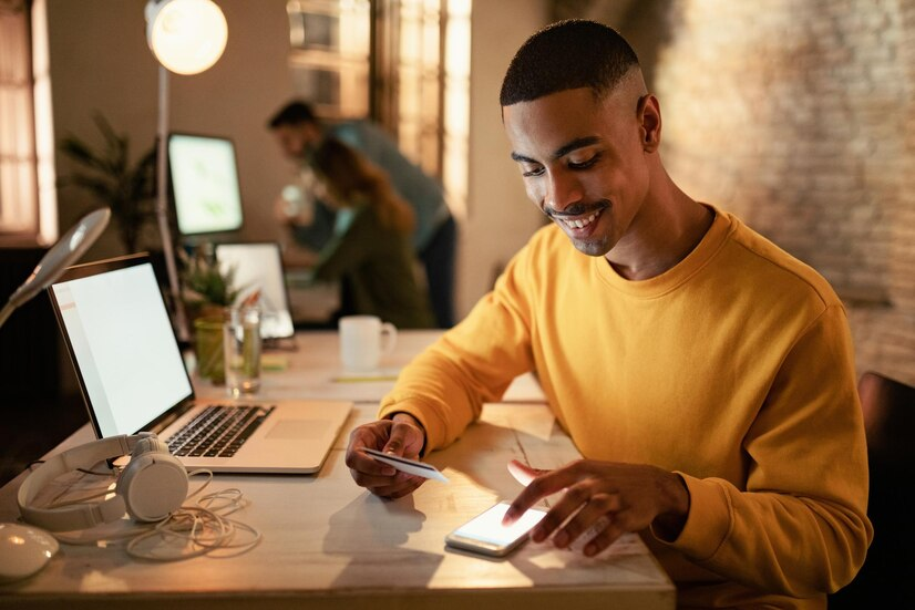 someone sitting at a desk with a laptop in front of him using his phone to pay for something as his digital wallet