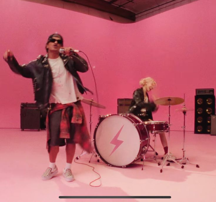 This  contains a picture of Rosé and  Bruno Mars standing in front of a pink wall with guitars and drums on the floor