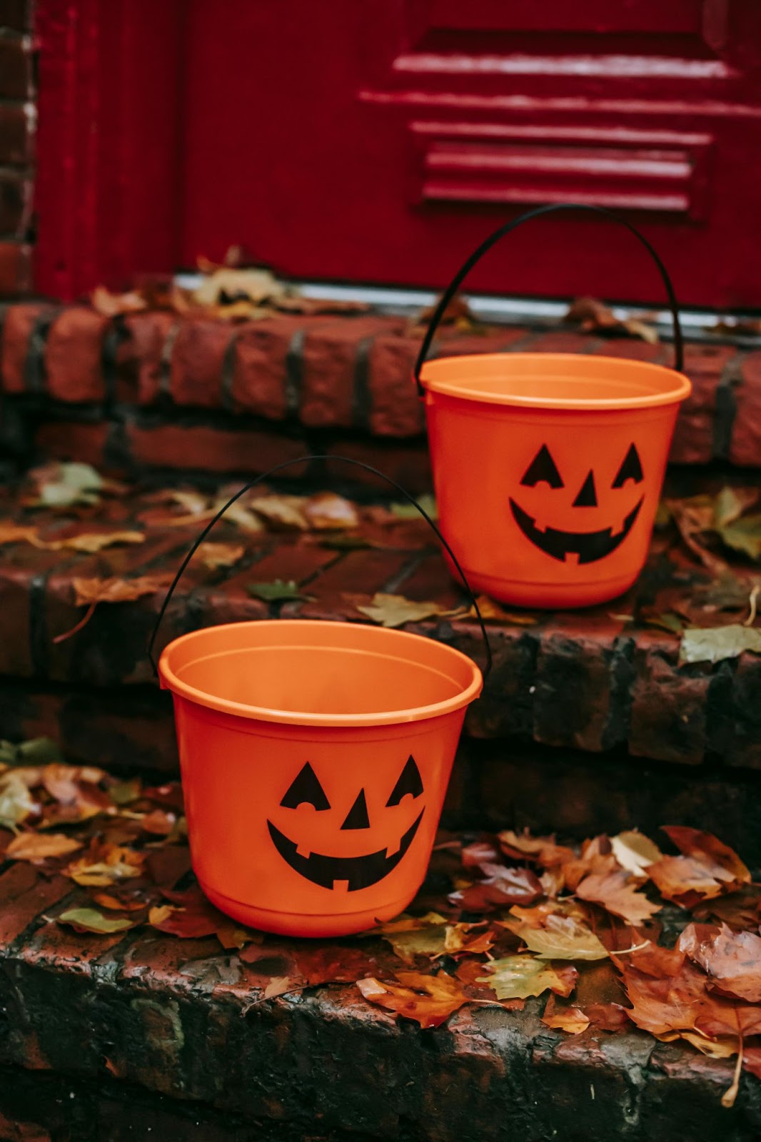 Two orange plastic halloween candy buckets that look like carved pumpkins