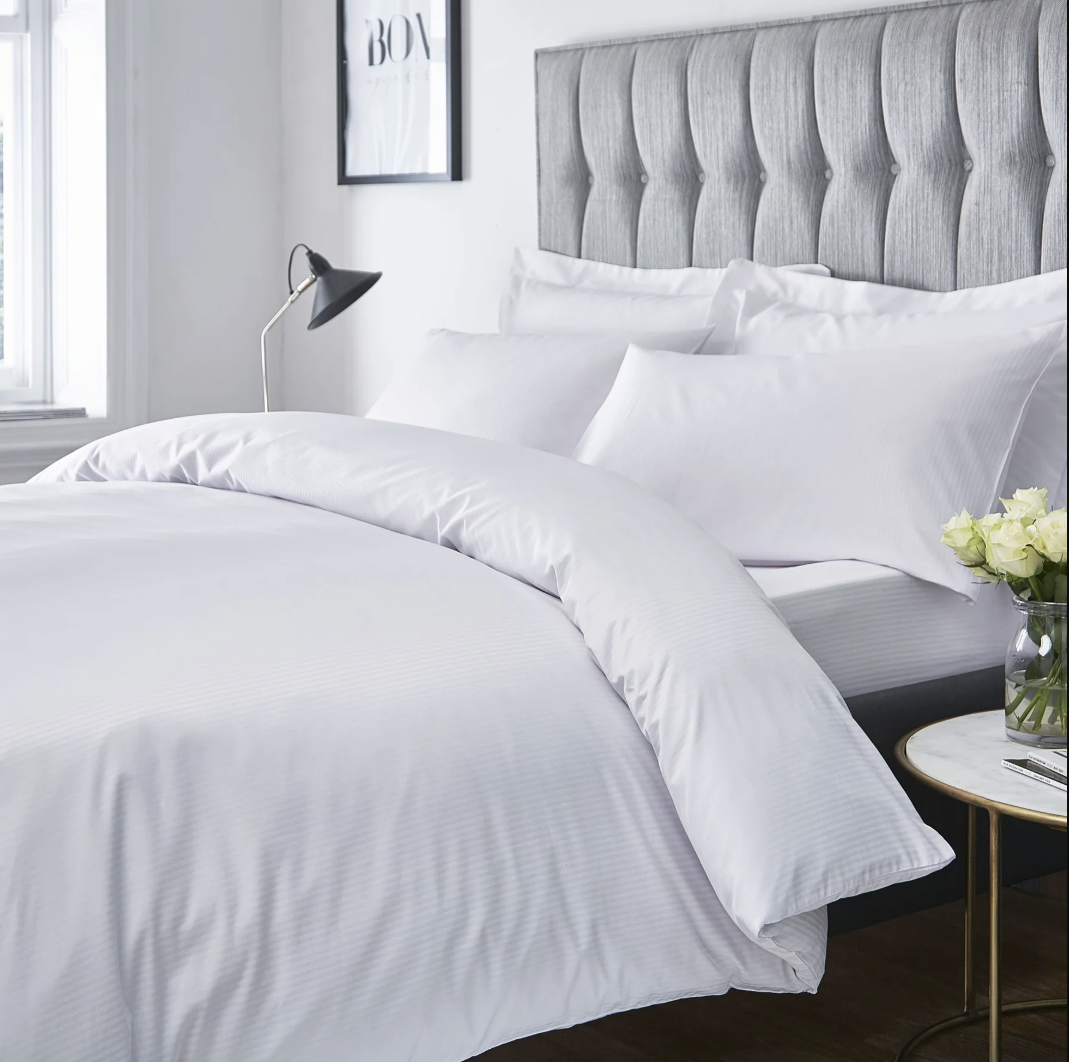 Crisp white bedding folded nearly across a bed with a lighter décor scheme.