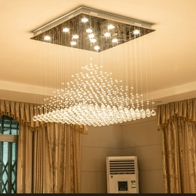A contemporary living room chandelier, spangled with golden lights, falls gently from the ceiling niche as an elegant waterfall feature.
