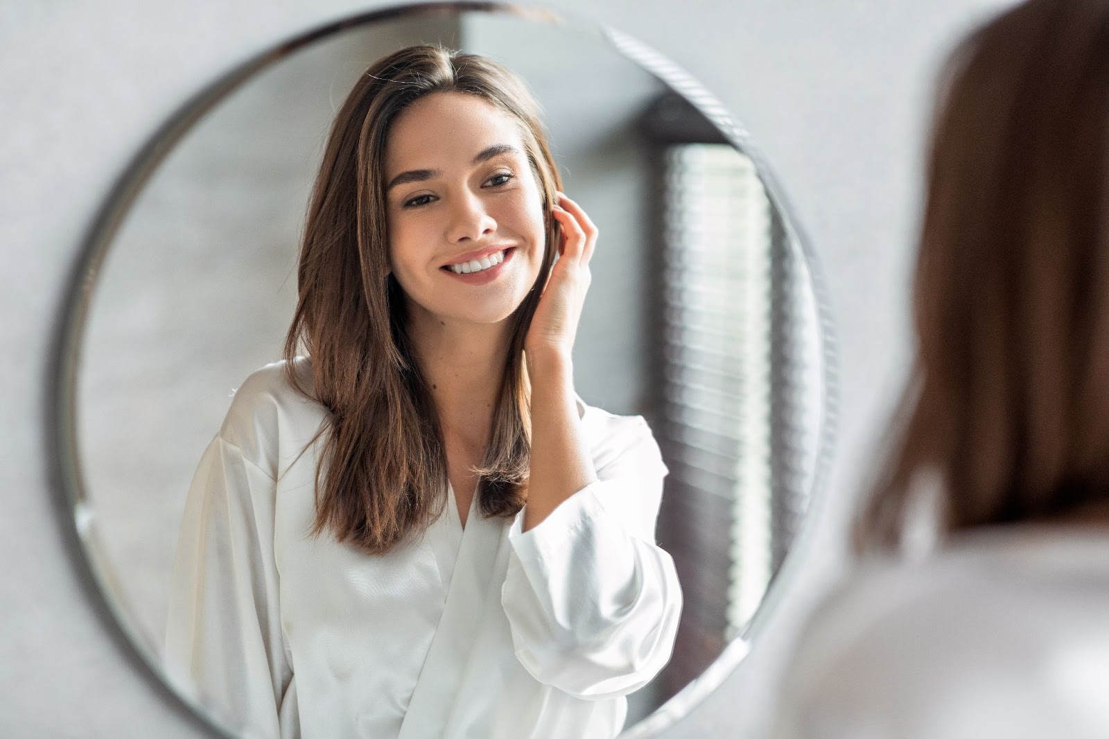 A woman looking at herself in the mirror admiring the results of her skin care treatment.