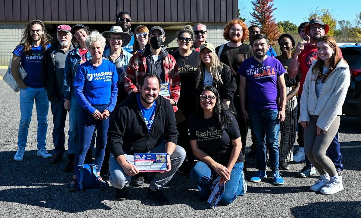 Rep. Tlaib and Rep. Wegela kneel in front of a group of about 20 canvassers.