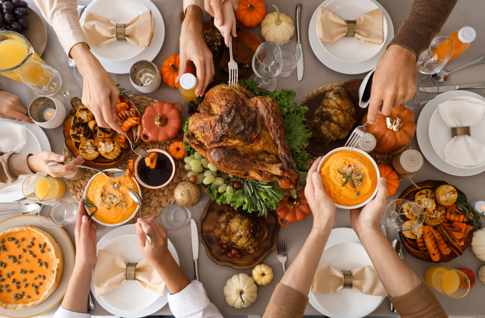 An overhead shot of a Thanksgiving table full of different food while out-of-frame people pass dishes to one another.