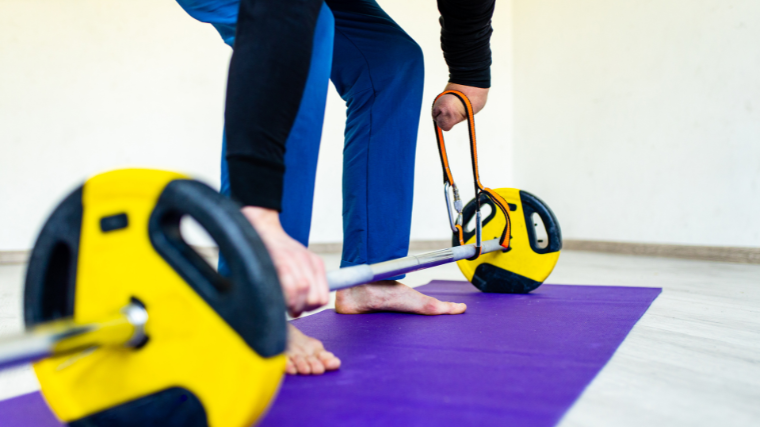 An athlete performs a deadlift on a yoga mat using an assistive device.