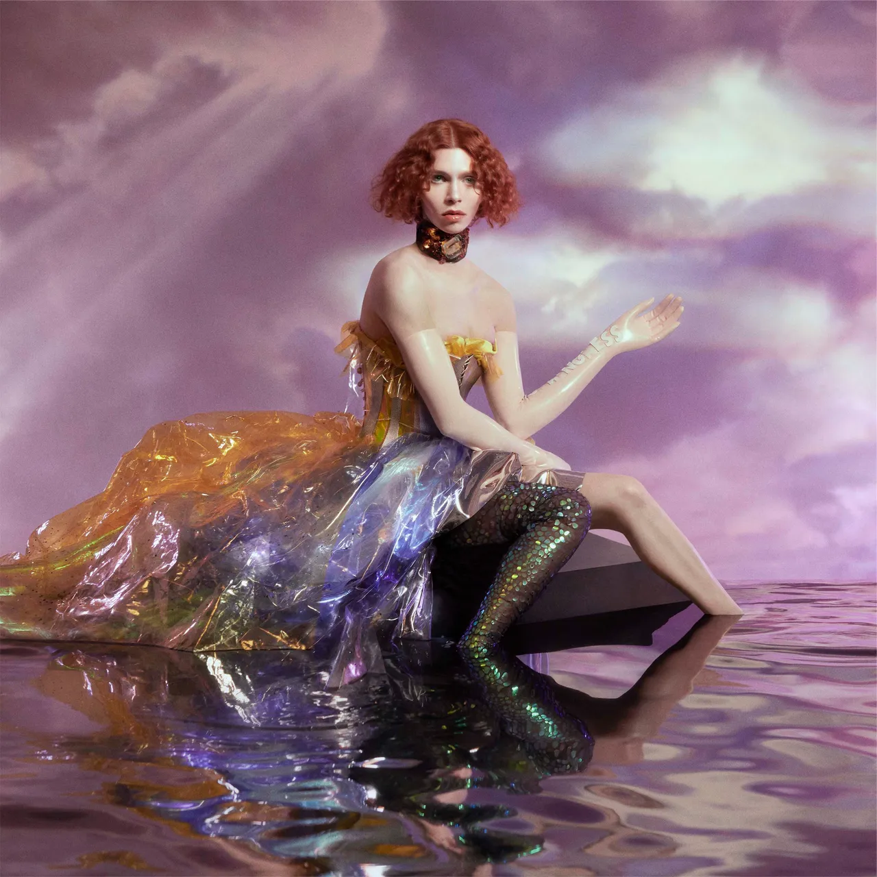 SOPHIE's 'Oil of Every Pearl’s Un-Insides' cover art featuring her with red curly hair in a colorful, translucent gown, seated on reflective water, surrounded by a pink and purple sky.