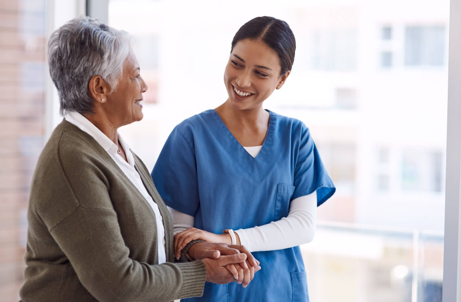 A caregiver smiling at an older adult while they walk together down a hall to help with balance problems.