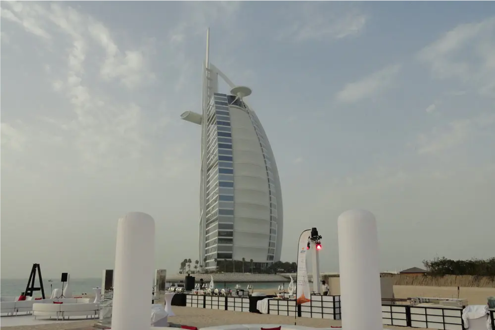 Beach wedding venue with curved white sofas, tall lamps, and Burj Al Arab in the background.