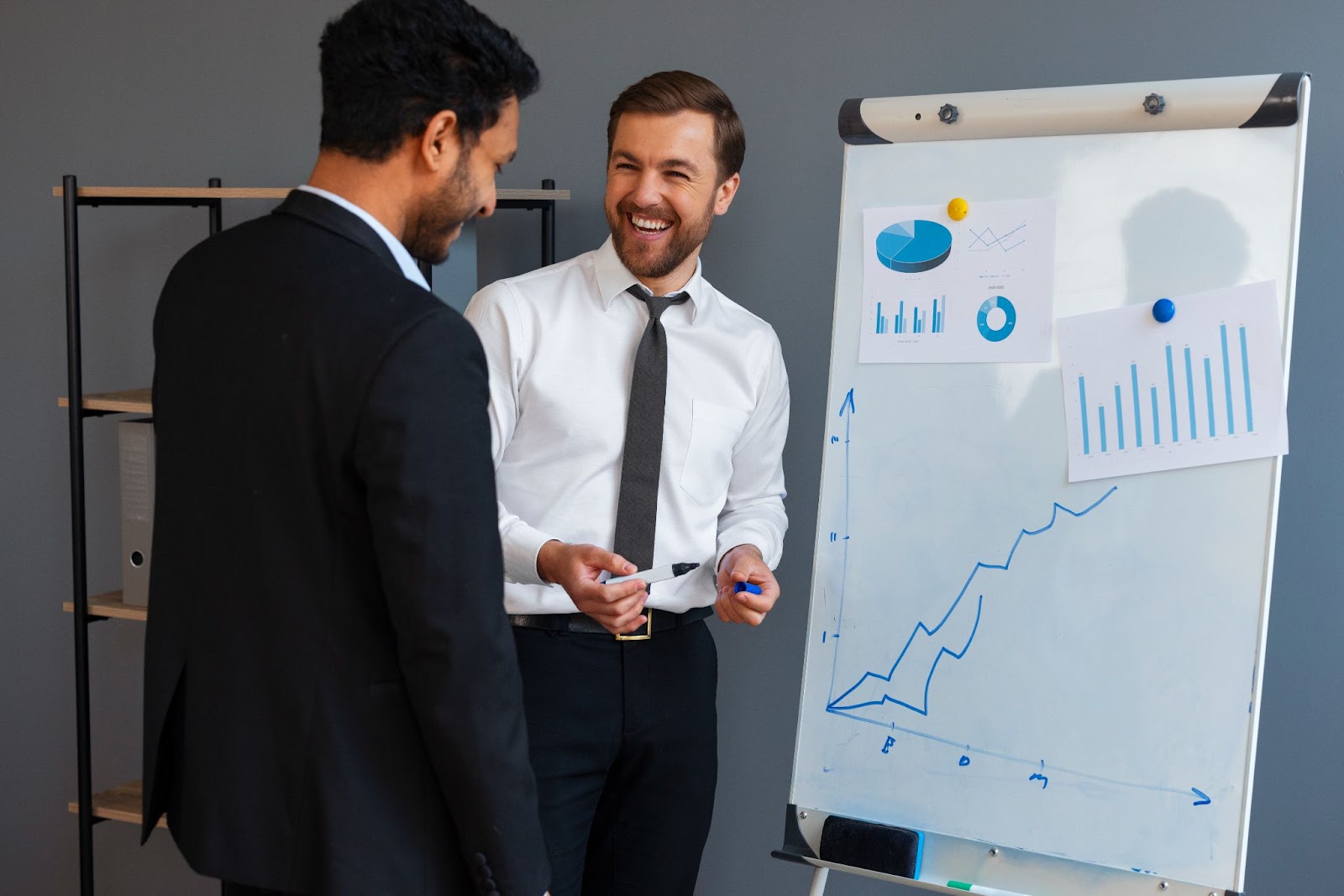 Two business professionals discussing data insights beside a whiteboard displaying charts and a rising performance graph, representing data-driven decision-making and talent analytics.