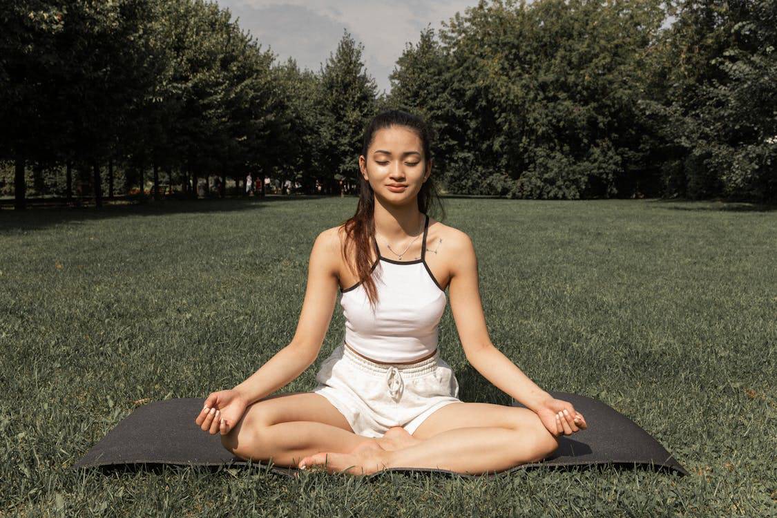 Mulher oriental de olhos fechados praticando Yin Yoga em um gramado verde, relaxando em uma postura profunda, ideal para iniciantes.