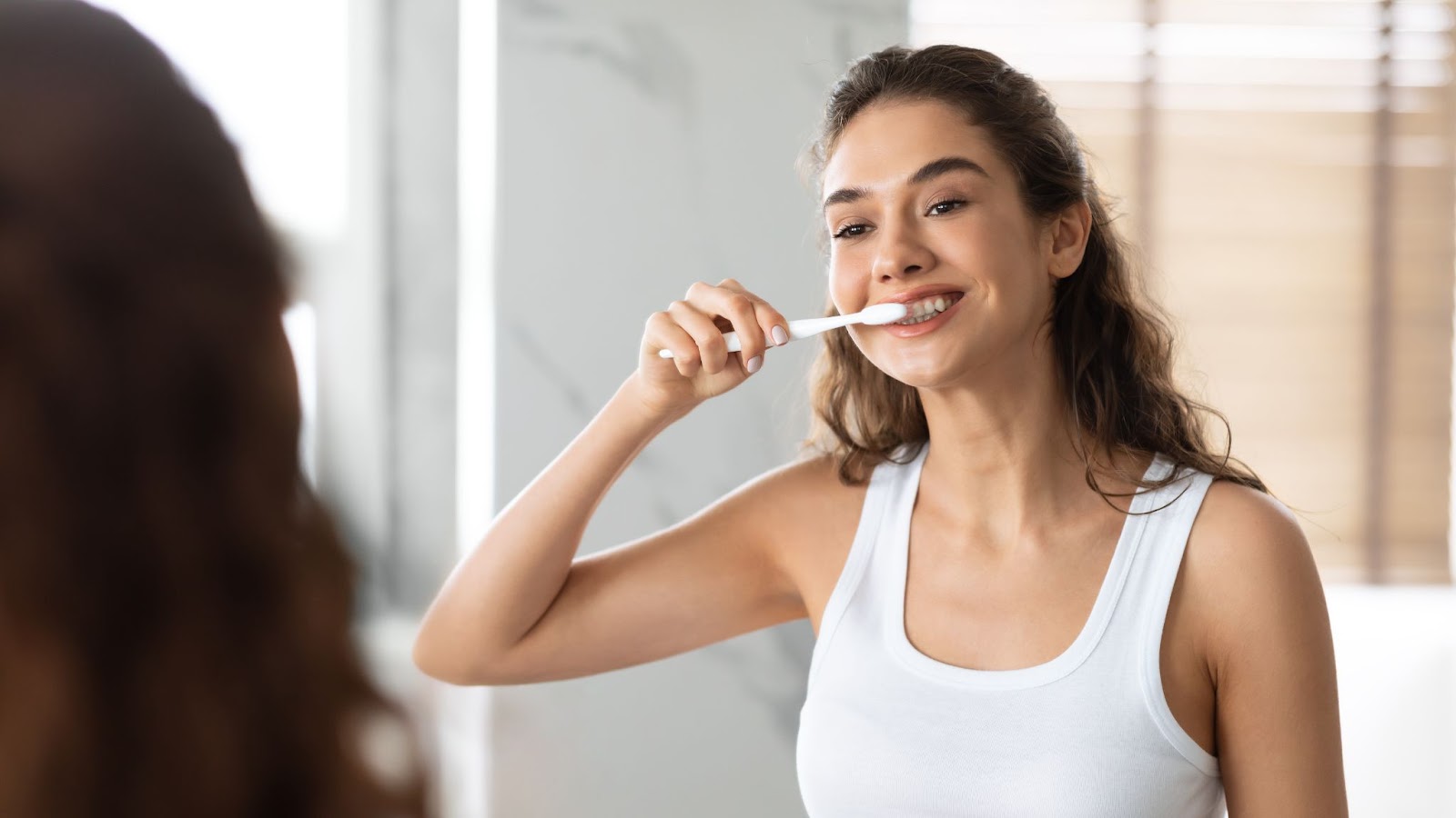 A woman looking in the mirror and brushing her teeth,