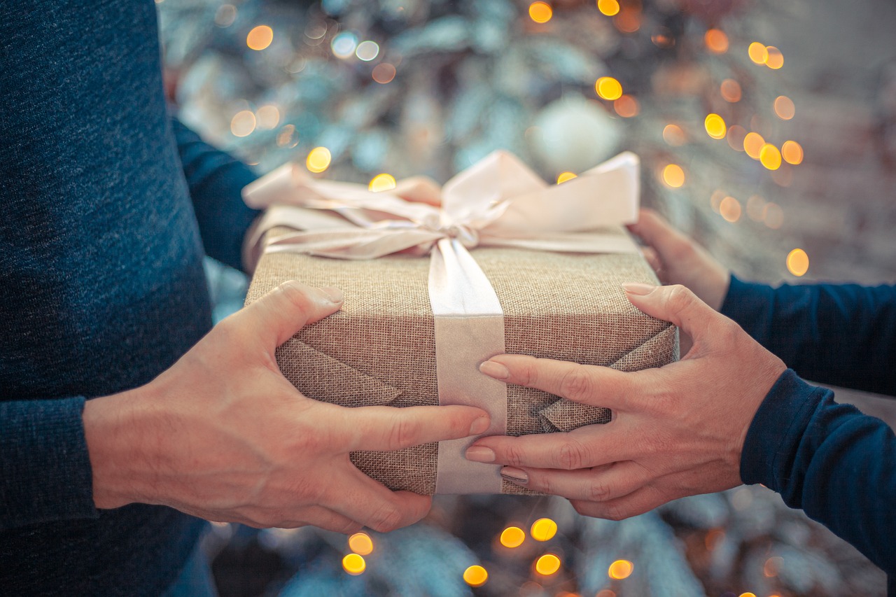 A person giving another person a gift. Blurred Christmas decor in the background. 