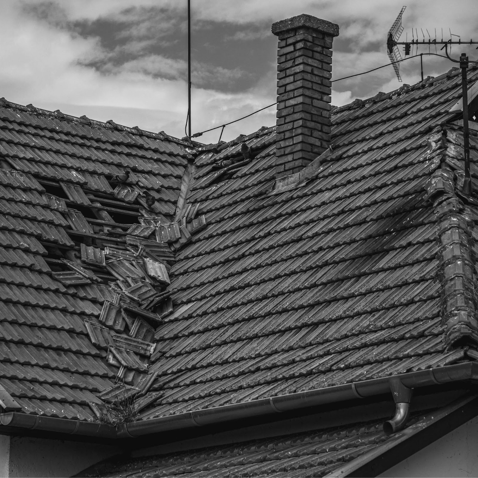 A damaged roof with missing tiles and broken tiles.