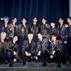 This contains a group picture of the SEVENTEEN members in black and gold outfits posing for a photo on stage