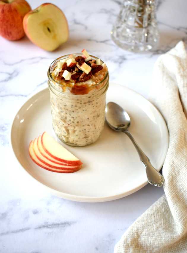 Overnight oats in a jar topped with diced apples, pecans, and caramel, served with apple slices.