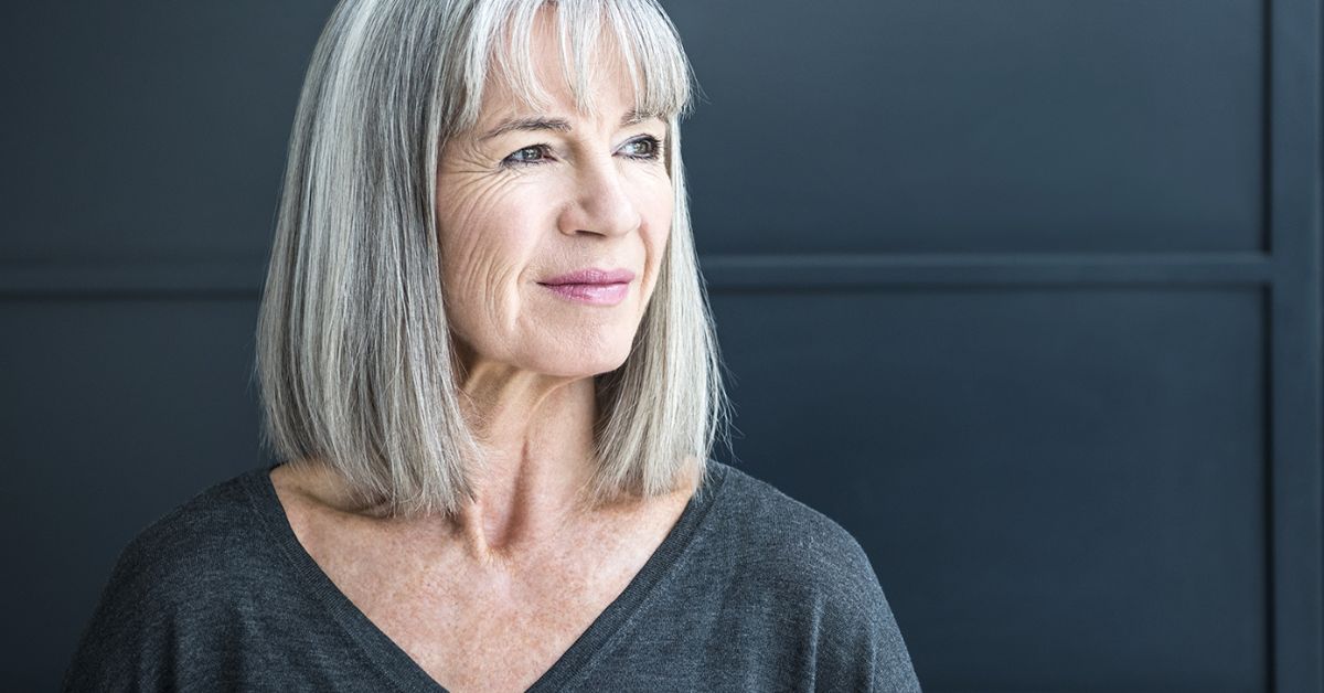 A woman with straight gray hair wearing a black shirt, exuding elegance and confidence in her appearance.