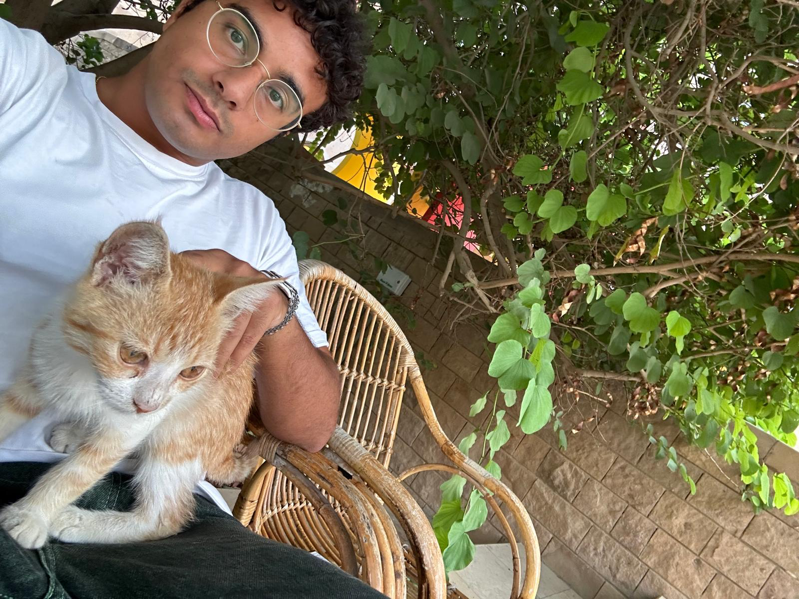 Man holding an AUC cat while seated under a bush