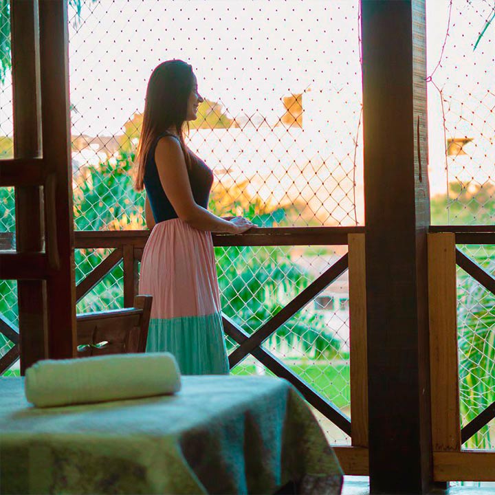 Mulher contemplando a paisagem ao entardecer, em uma varanda, com um vestido elegante e colorido.