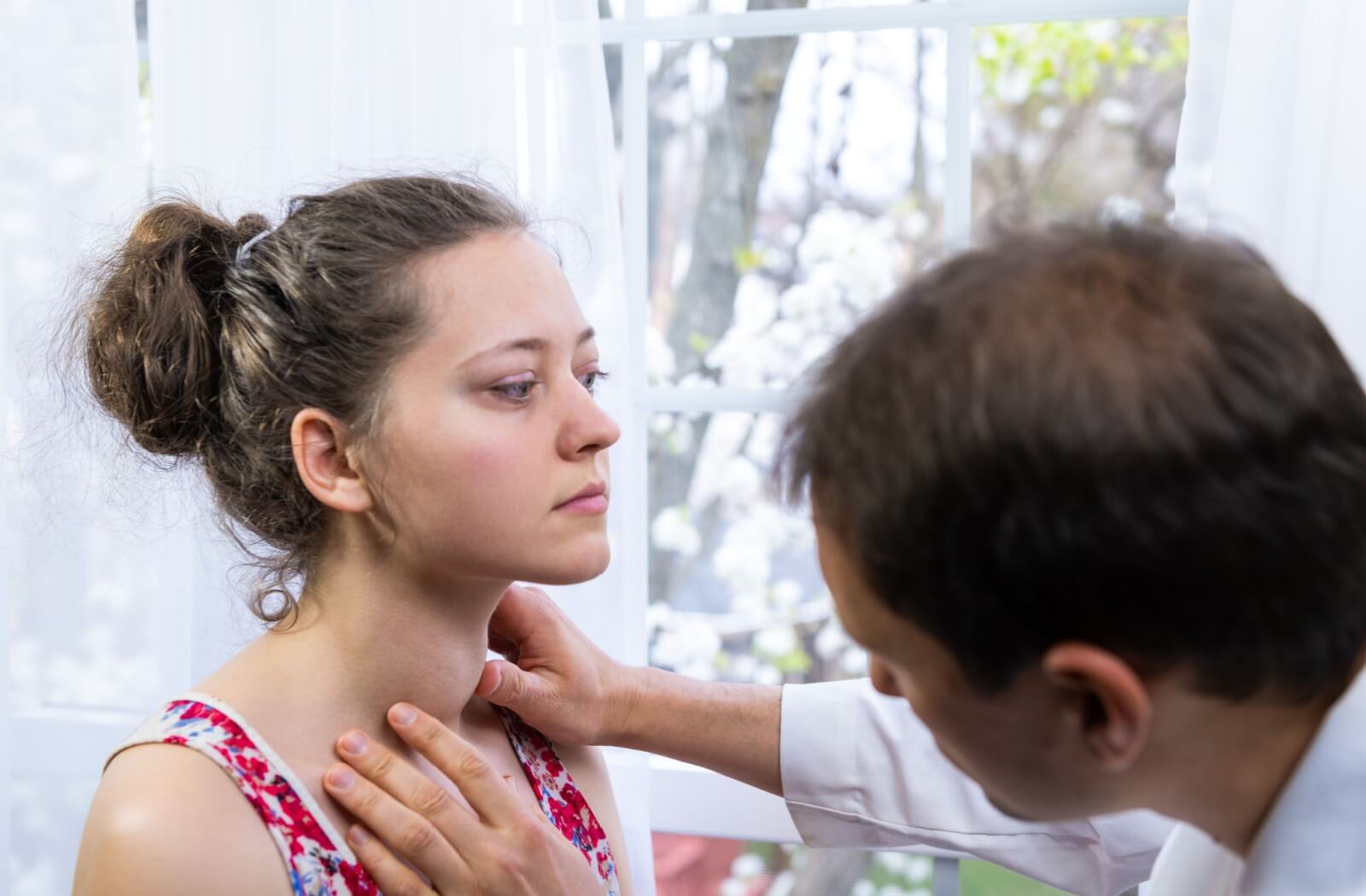 A doctor inspects a patient's swollen neck and thyroid gland due to hyperthyroidism.