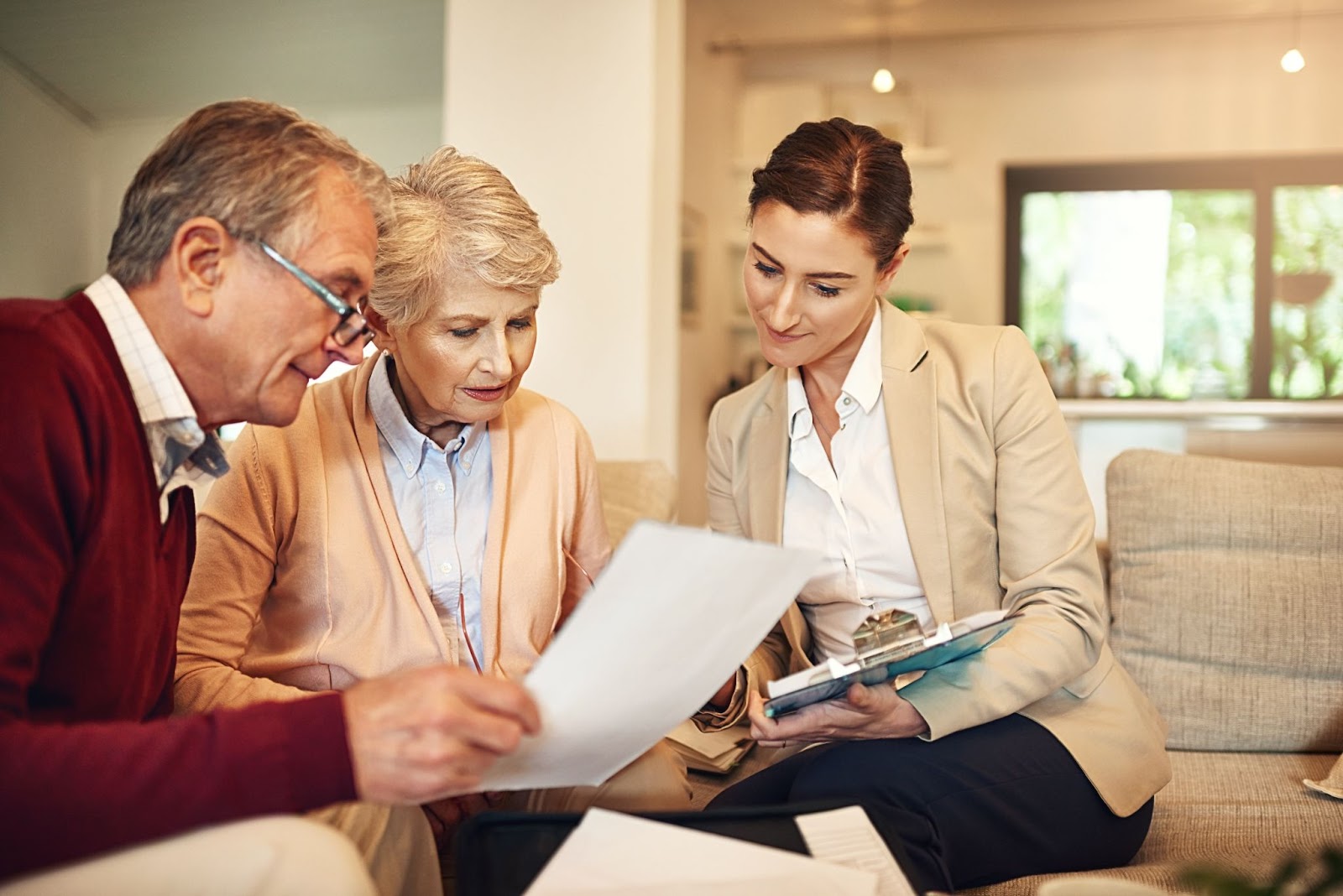 A financial advisor and older couple sitting on a couch looking at documents in early financial planning for assisted living.