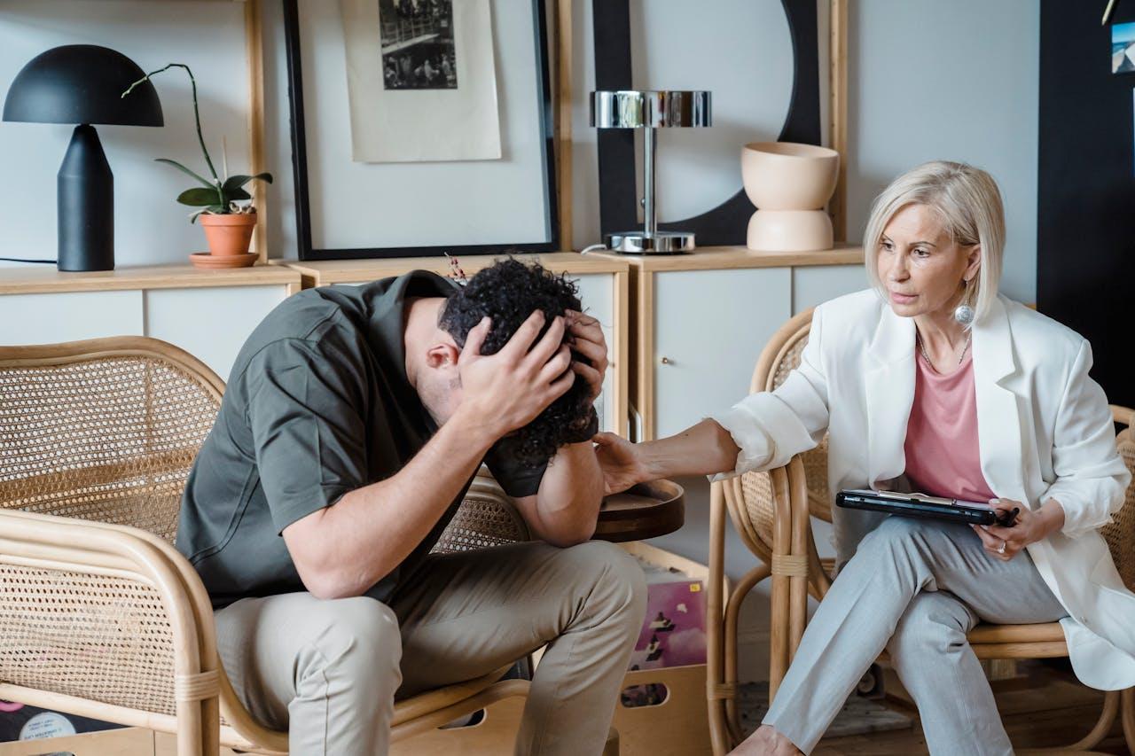 Homem preocupado com as mãos na cabeça e a psicóloga conversando com ele durante a sessão.