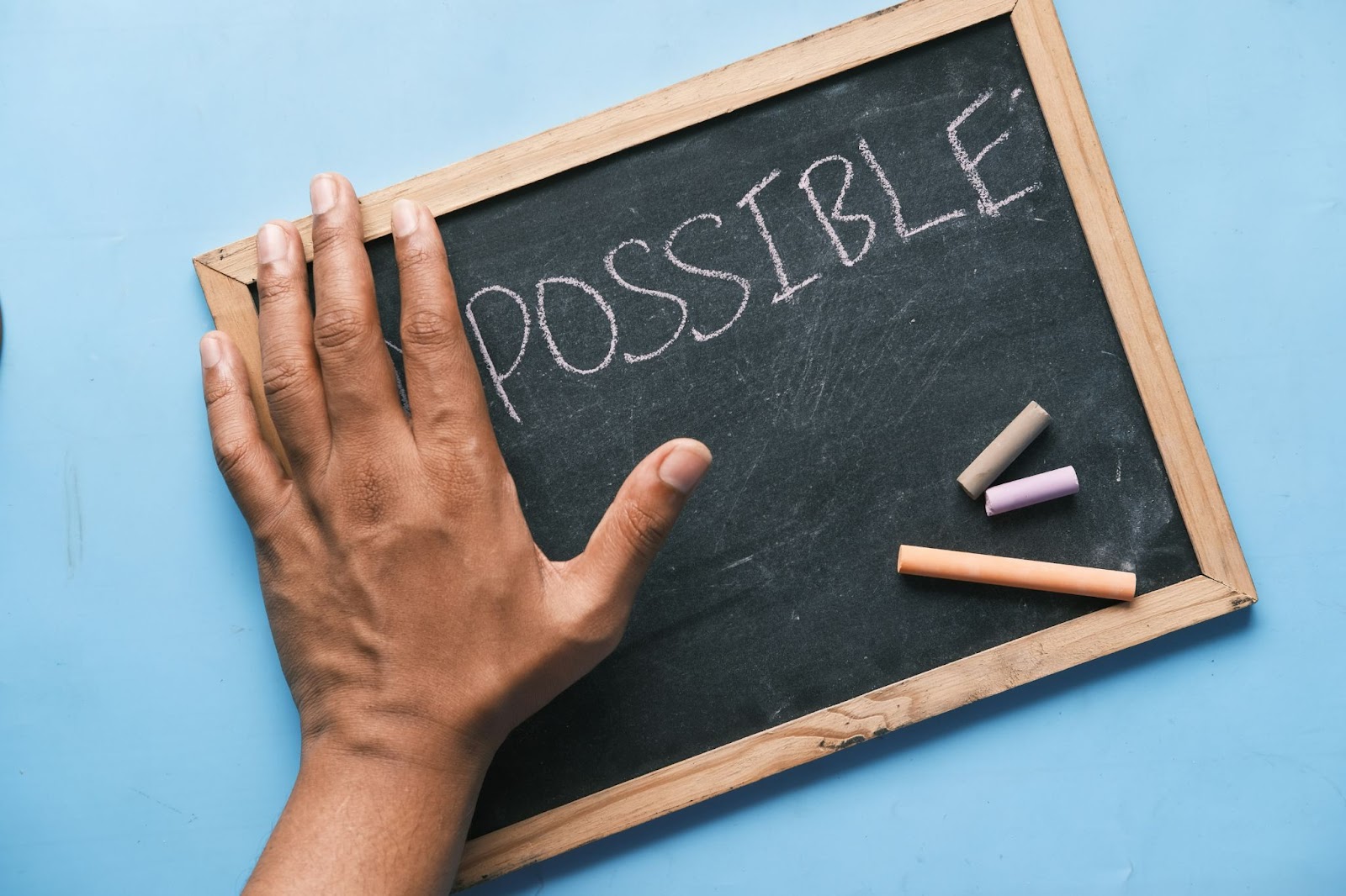 A hand blocking out the letters “im” before the word “possible” written on a small chalkboard.