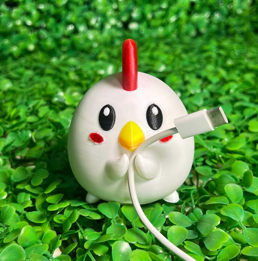 Cute 3D printed chicken cable holder organizing a white USB charging cable on green leafy background

