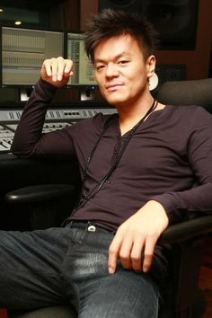 This  contain J.Y. Park sitting in front of a mixing desk with his hand on his head and looking at the camera