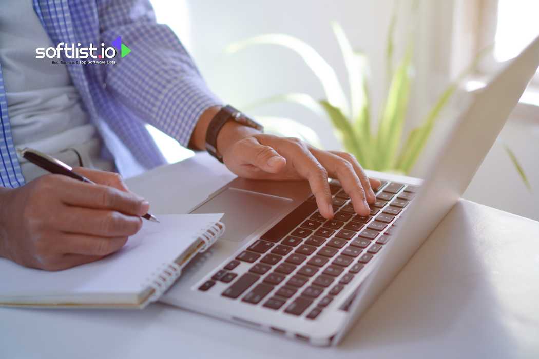 Person writing in a notebook while using a laptop