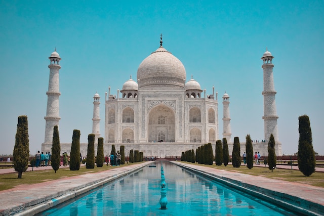 A view of the Taj Mahal, an architectural masterpiece in Agra, showcases its iconic white marble dome and minarets under a clear blue sky.