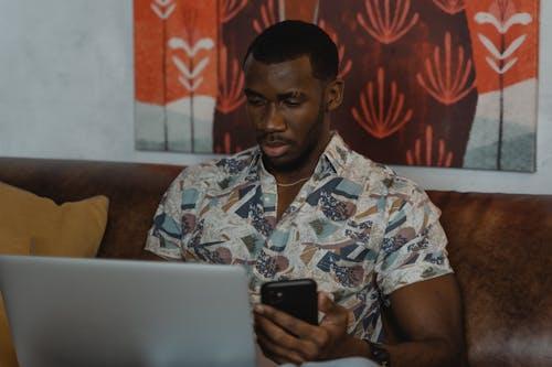 Free Man in White and Blue Floral Button Up Shirt Holding Black Smartphone Stock Photo