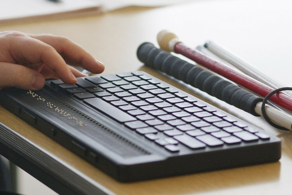 A braille keyboard for computer placed on a wooden table, accompanied by mobility aids like white canes