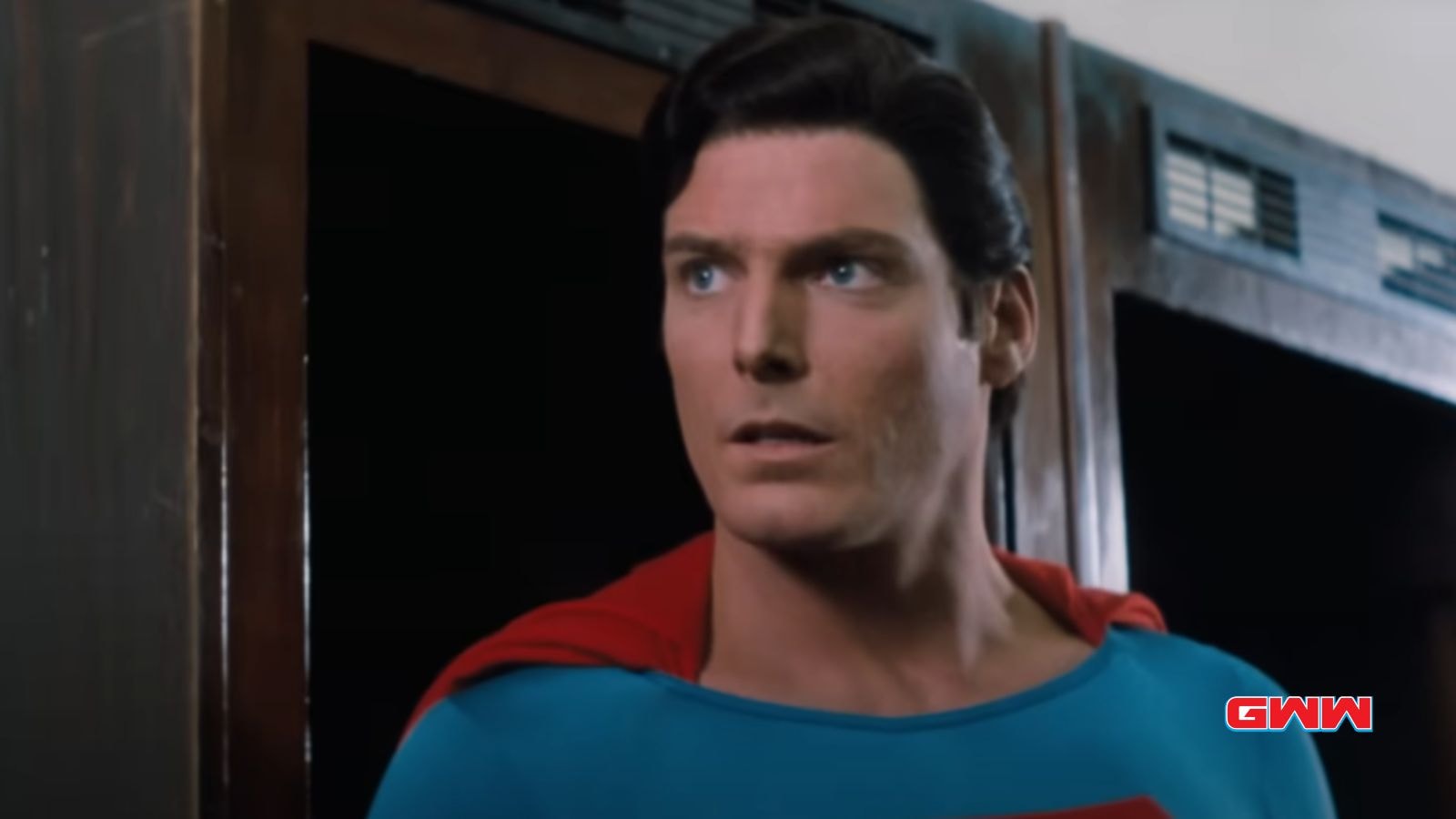 Christopher Reeve in Superman costume looking surprised inside a room.