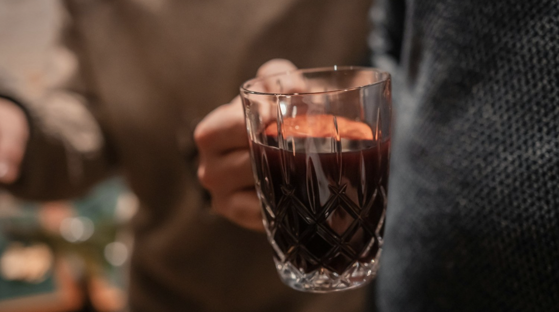 A man is holding a crystal mug filled with glogg garnished with fruit
