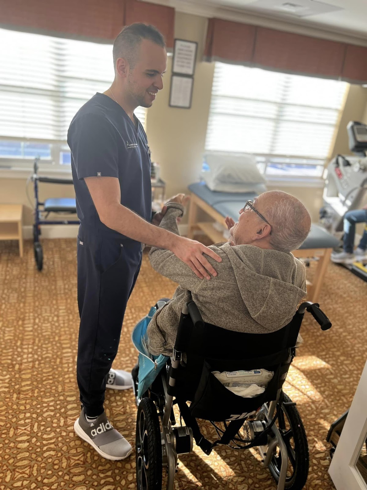 Village Walk's Dr. Amir Amrami with his hands on the shoulder of an elderly man who is in a wheelchair