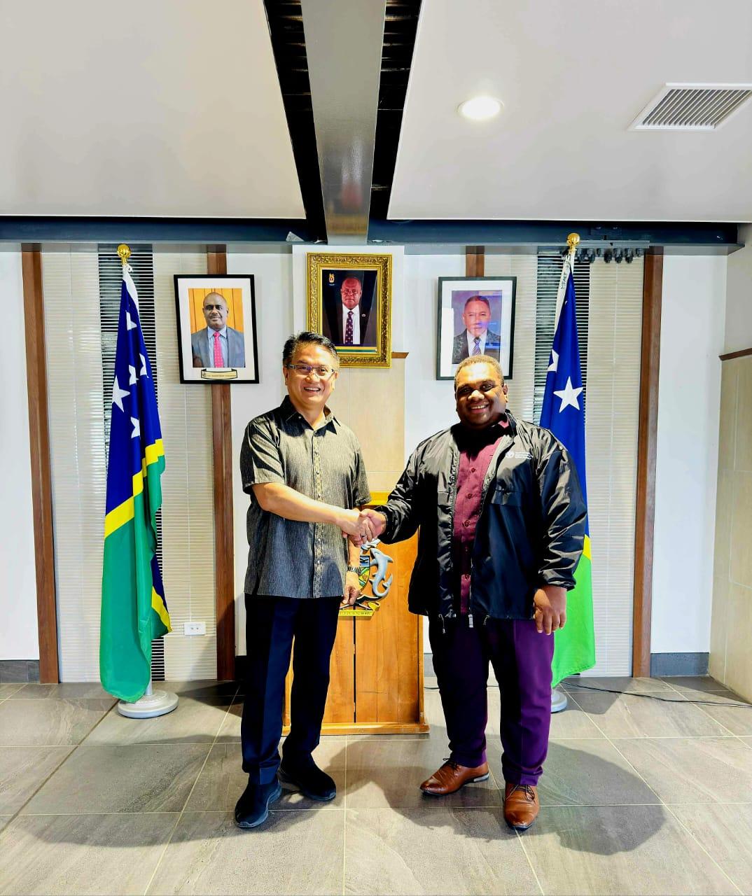 Two men shaking hands in a roomDescription automatically generated