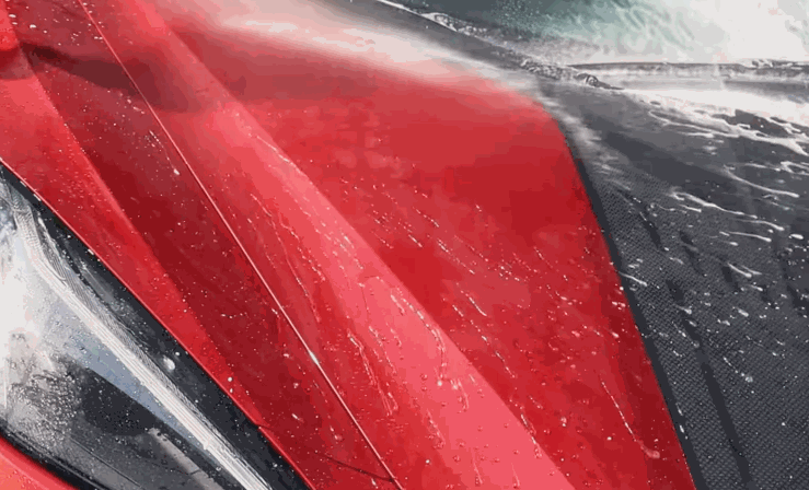 Water sprays across a vibrant red car hood during a wash, emphasizing the glossy finish and smooth contours of the vehicle