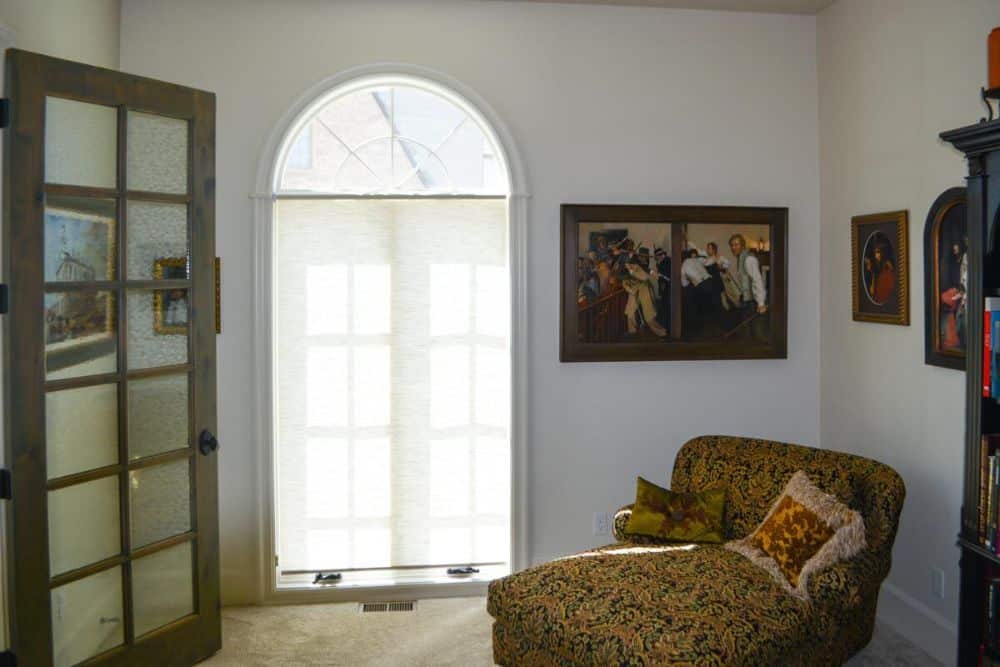 The home office includes a lounge chair and an arched window that invites natural light in.