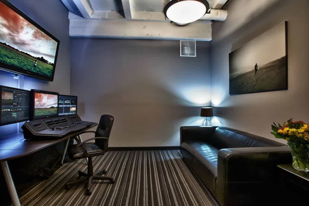A modern professional video editing and post-production studio with multiple monitors, a control surface, and comfortable seating